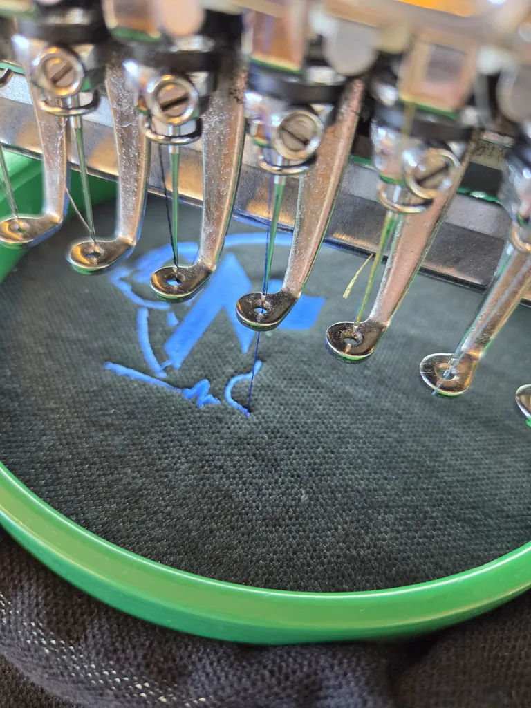 Embroidery needles stitching a blue design onto fabric in a green hoop